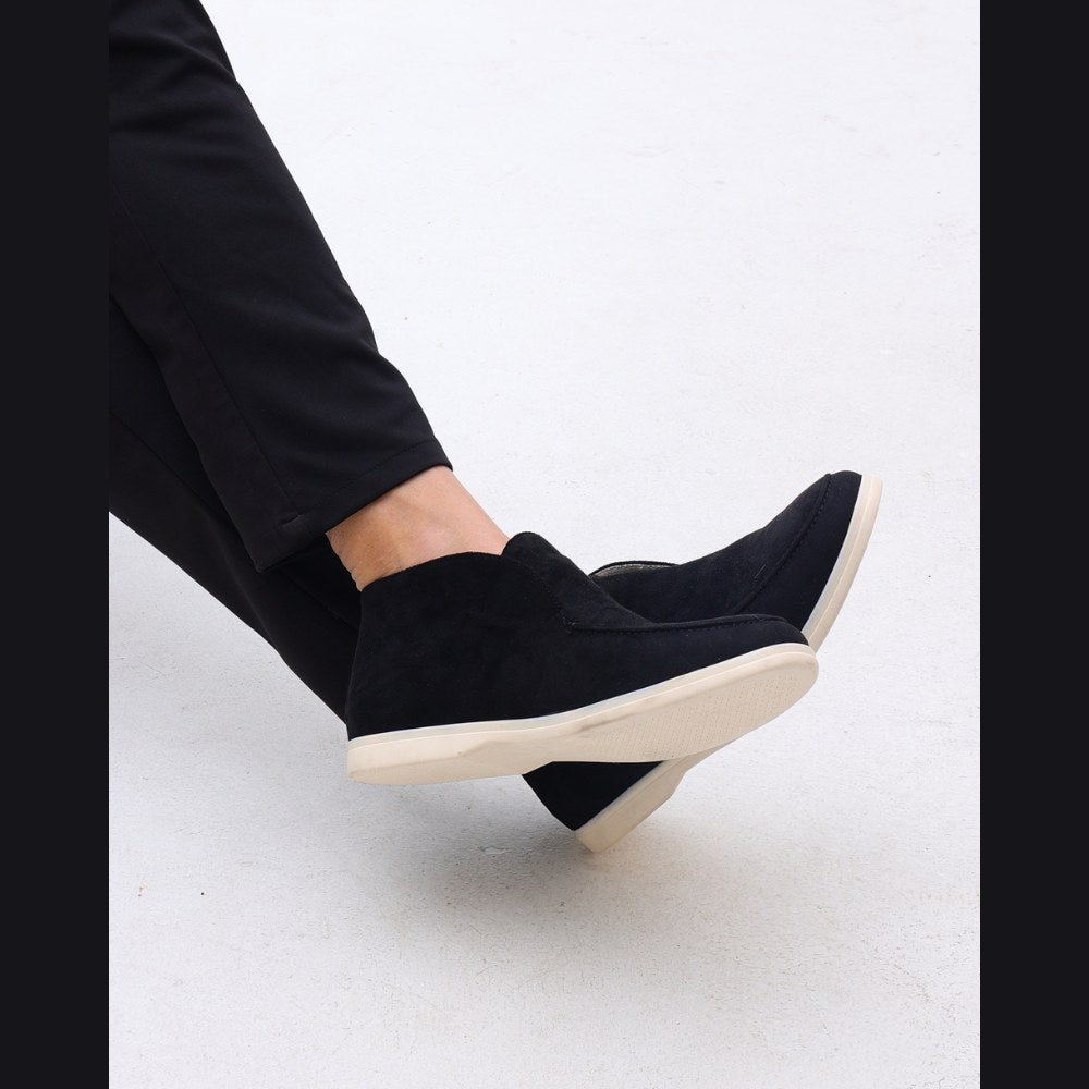Lower-leg view of the darker high-top suede slip-ons worn with black trousers