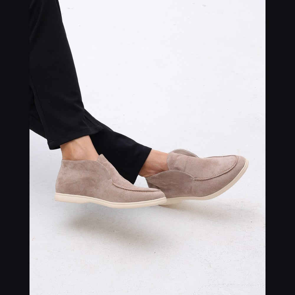 Lower-leg view of the taupe high-top suede slip-ons worn with black trousers
