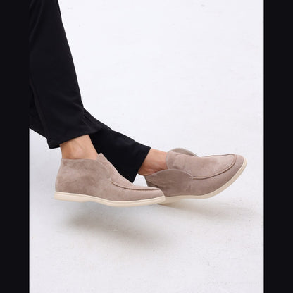 Lower-leg view of the taupe high-top suede slip-ons worn with black trousers